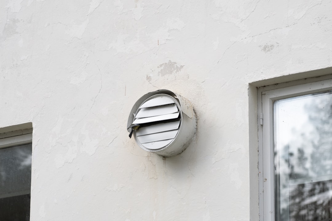 a-round-metal-vent-on-a-white-stucco-wall-lnemfrmg7yc